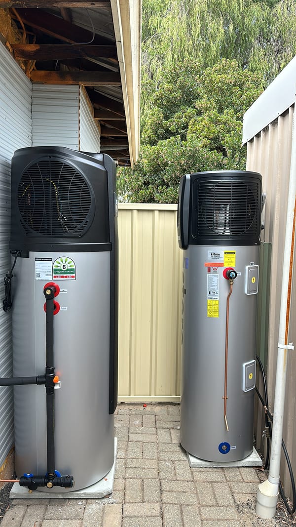 Plumber installing a Rheem hot water system against an external brick wall