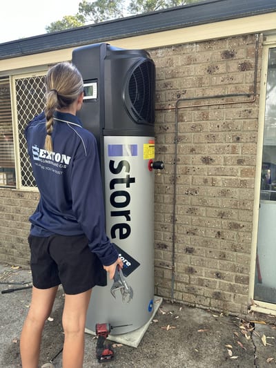 Plumber installing a Rheem hot water system against an external brick wall